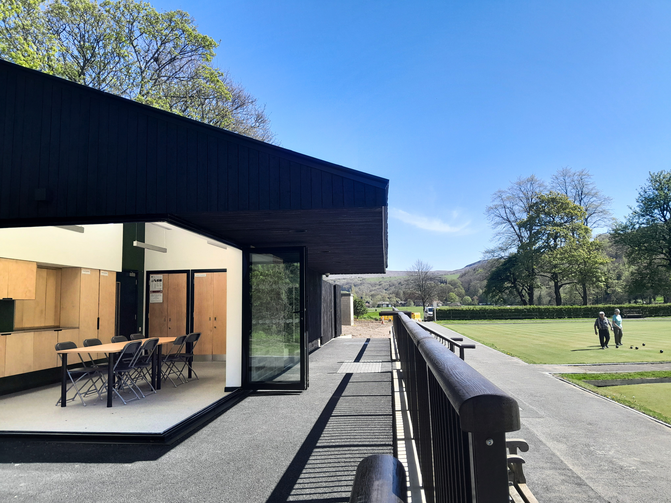 Photo of the Pavilion with bifold doors open, and people bowling on the greens in the sunshine